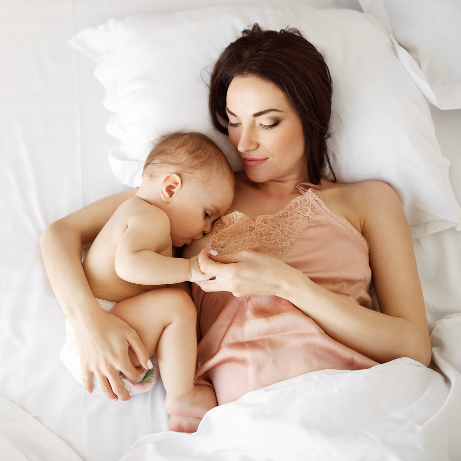 Young beautiful mom breastfeeding her newborn baby lying in bed at home. From above. Copy space.