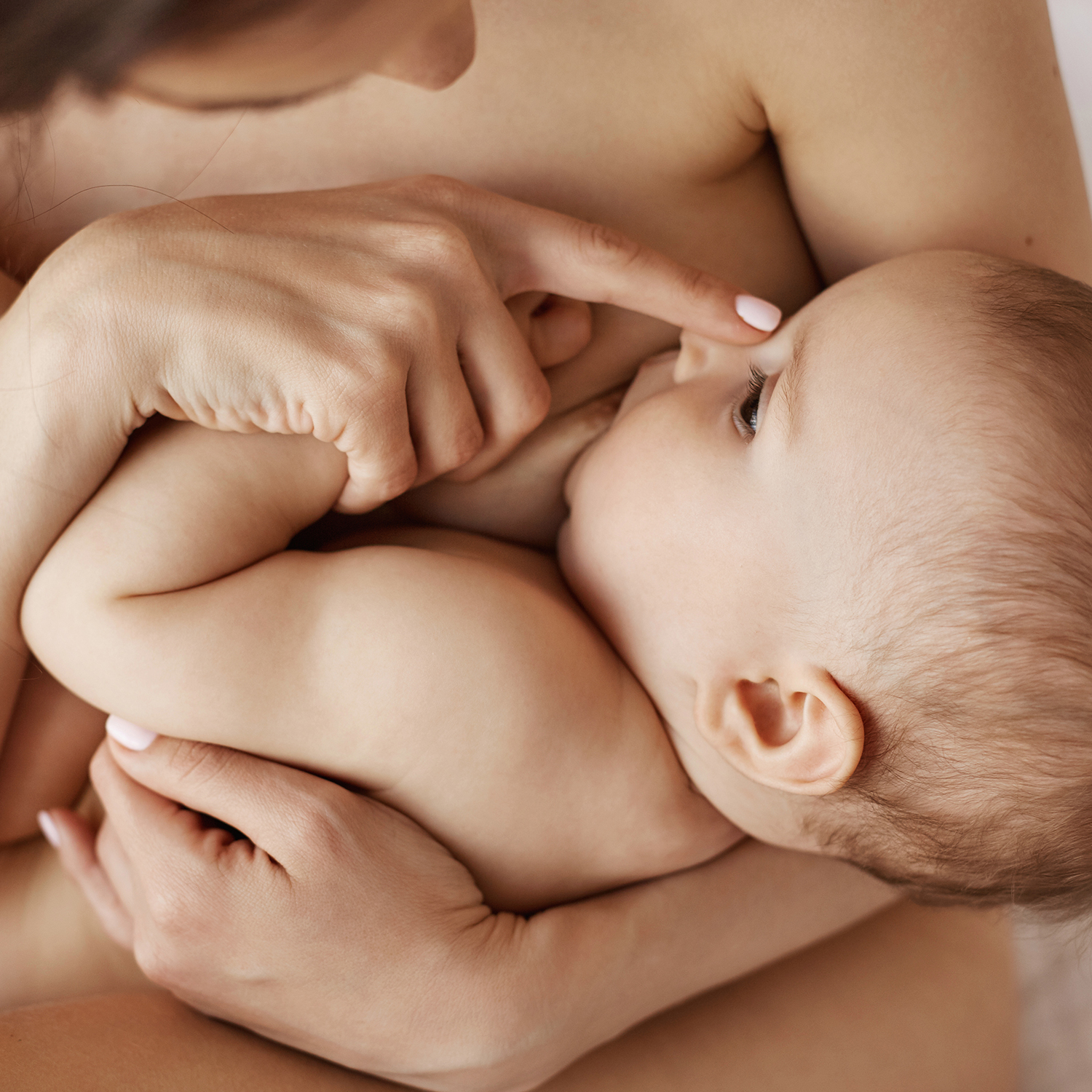 Young tender nude mother breastfeeding hugging her newborn baby sitting in bed at morning. Copy space.