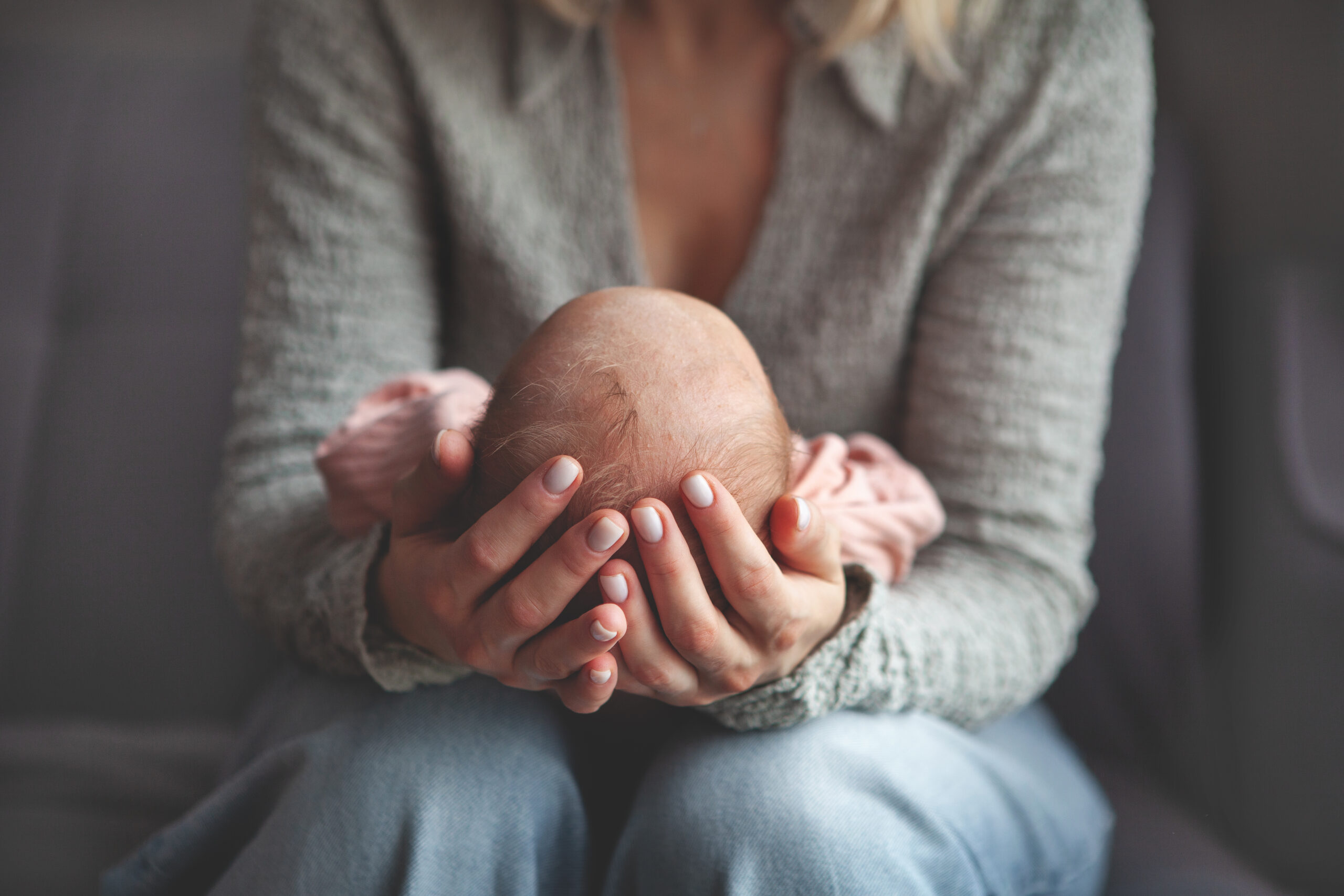 Close up mom gently cradling and rocking newborn baby in arms. Focus on hands holding baby, capturing tender, intimate moment of maternal care and love