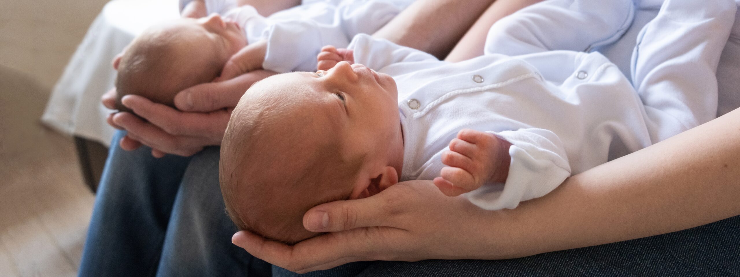 Newborn twins on the bed, in the arms of their parents, on a white background. Life style, emotions of kids. Multiple pregnancy. The large family