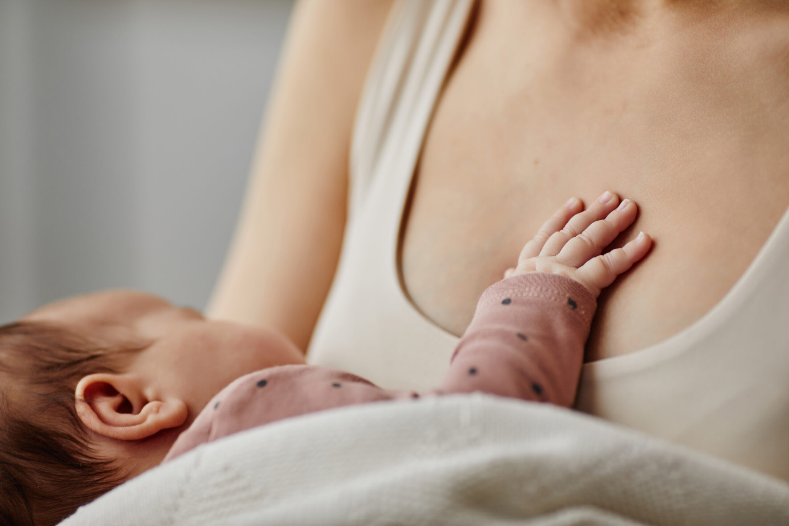 Close up shot of baby in white coating putting hand on mother chest during sleep, focus on baby hand, copy space